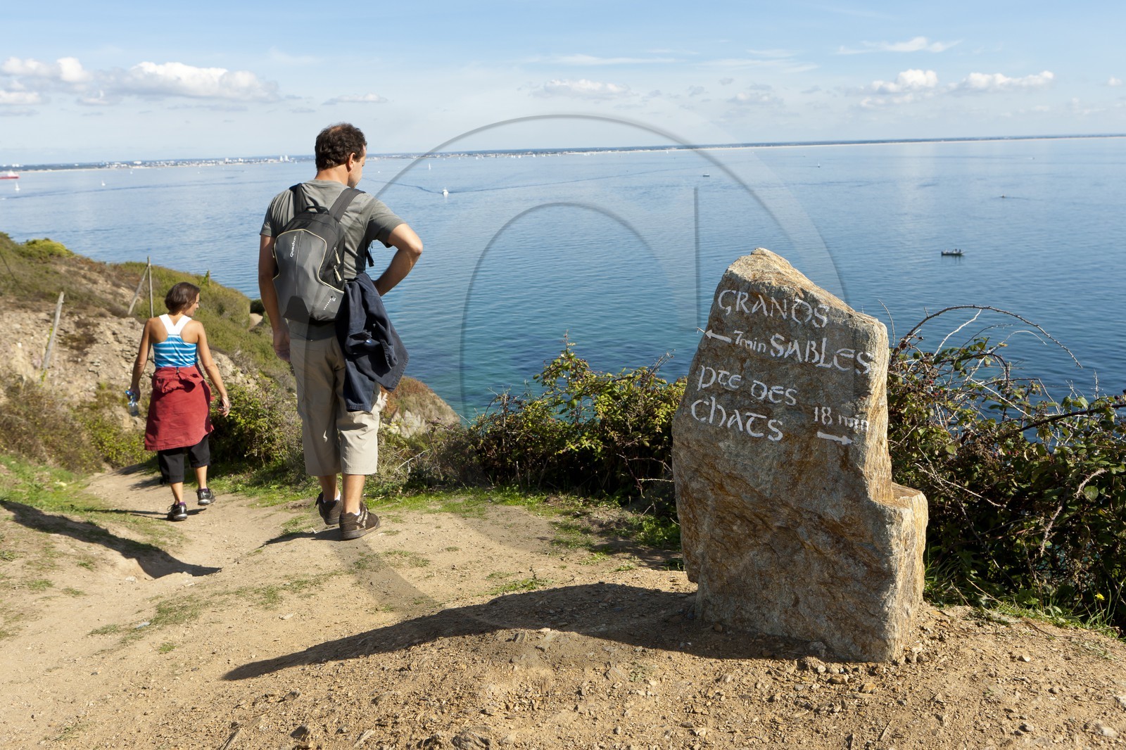 Un couple de randonneurs empruntant un des nombreux sentiers côtiers de l' ile de Groix. Un rocher dressé tel un menhir est utilisé comme panneau indicateur.A couple of hikers along one of the many coastal paths of the island of Groix. A rock stands as a menhir is used as a sign.